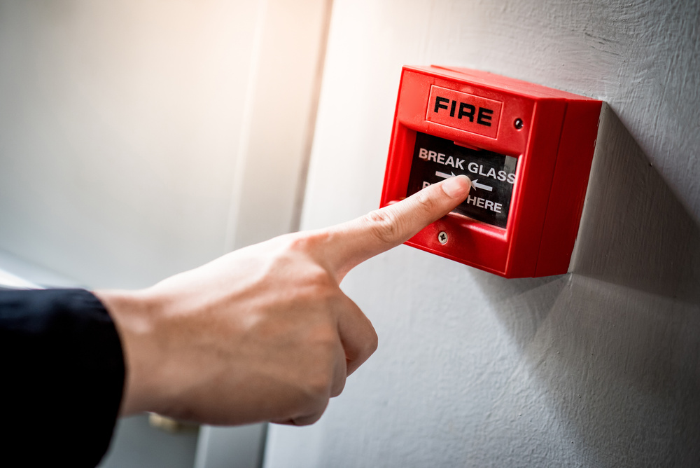 Hand pointing at a red break-glass fire alarm call point