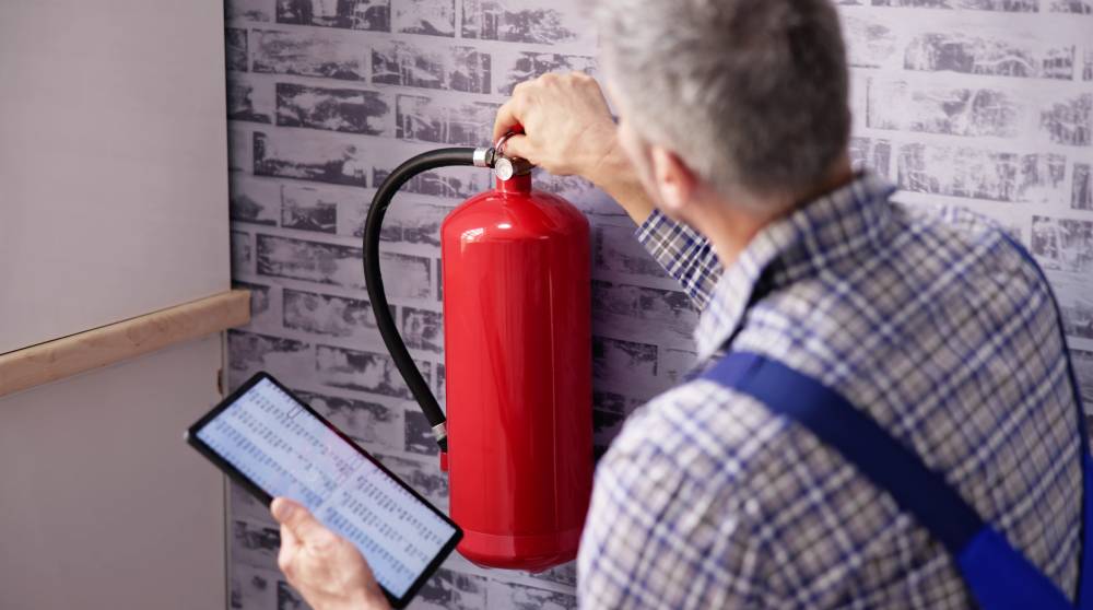 Technician with a tablet installing a wall-mounted fire extinguisher