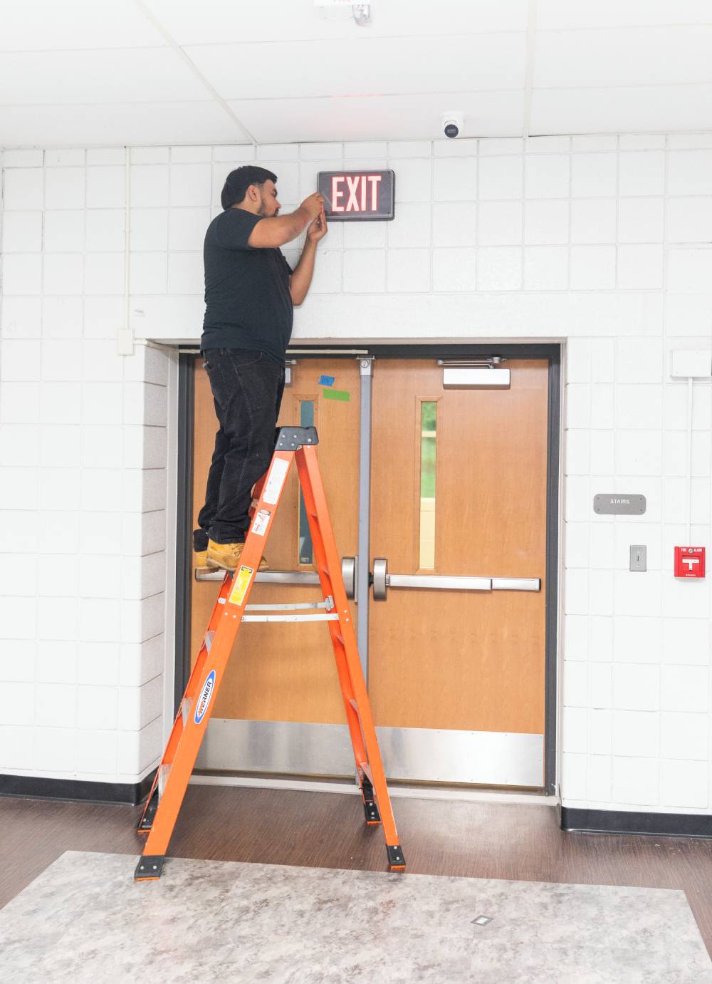 Technician on a ladder servicing an exit sign