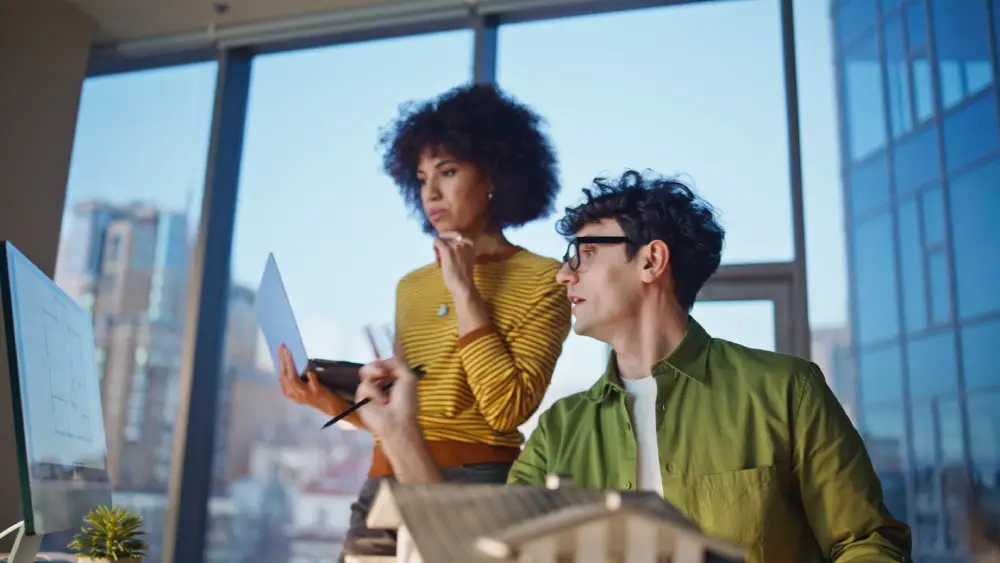 Two professionals reviewing plans by an office window