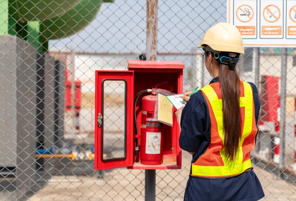 Technician in a hard hat and safety vest inspecting an outdoor fire hose cabinet