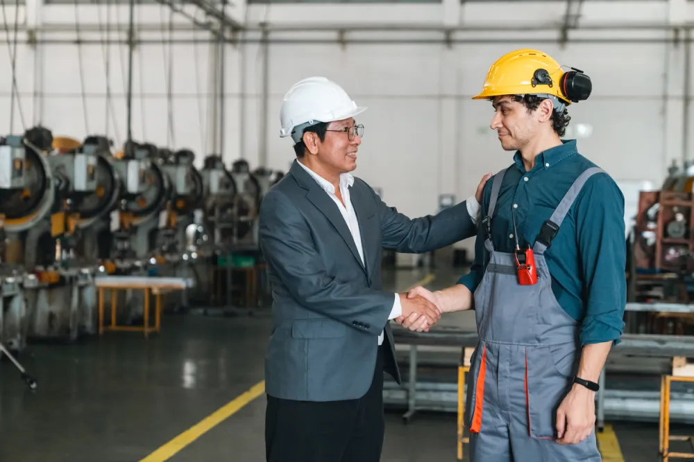 Manager and technician in hard hats shaking hands in a manufacturing facility