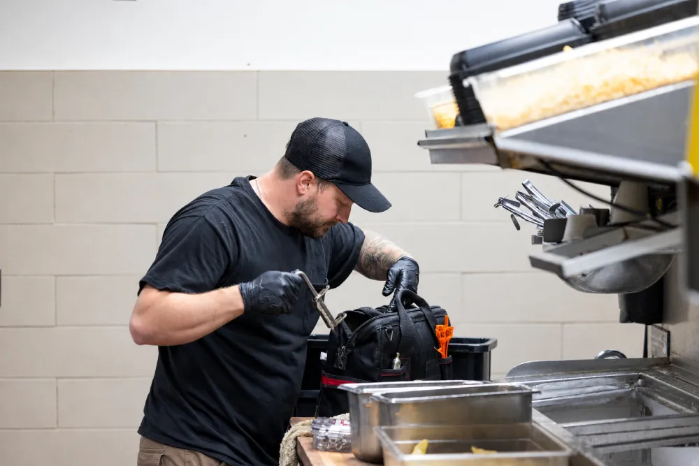 Technician inspecting fire suppression nozzles over commercial kitchen cooking equipment