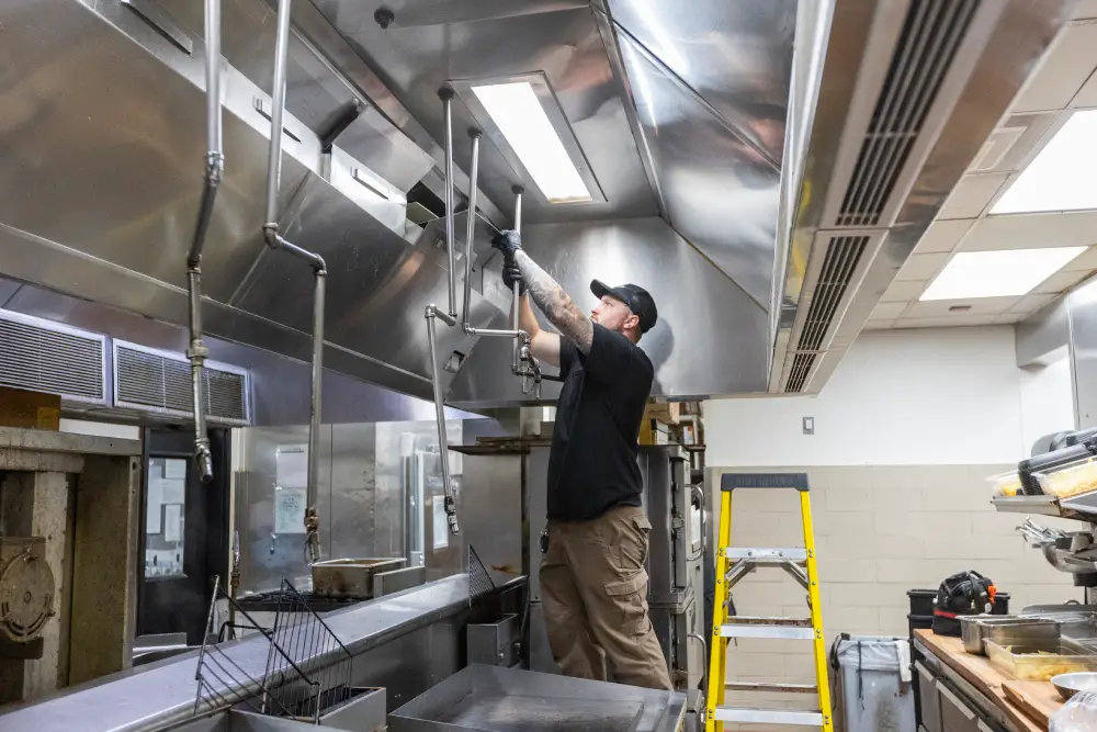 Technician inspecting a commercial kitchen exhaust hood suppression system