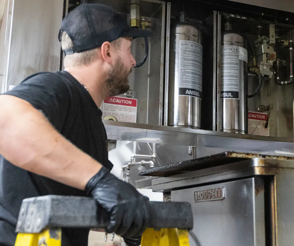 Technician on a ladder servicing kitchen fire suppression system cylinders