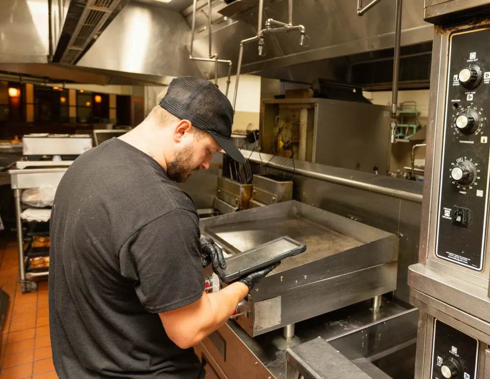Technician using a tablet to inspect commercial kitchen cooking equipment