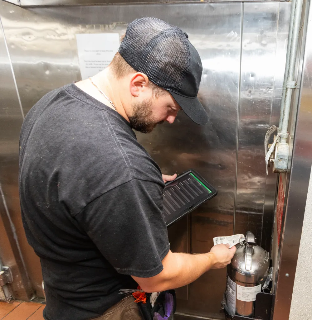 Technician inspecting a kitchen fire suppression system cylinder