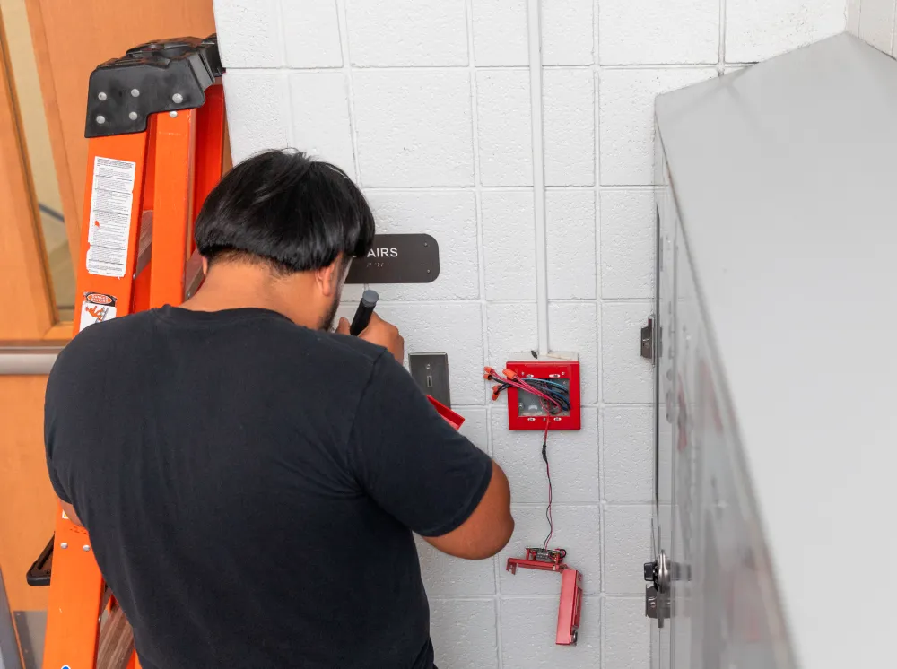 Technician on a ladder servicing a fire alarm device in a commercial building