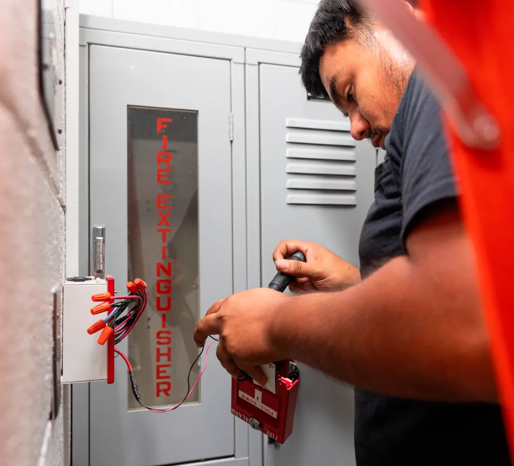 Technician servicing a fire alarm panel inside a utility room