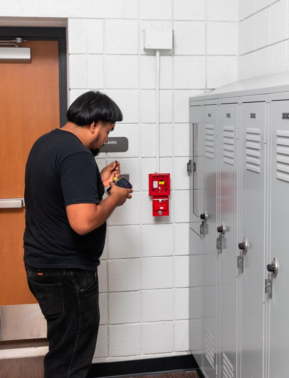 Technician inspecting a fire extinguisher in a hallway beside lockers