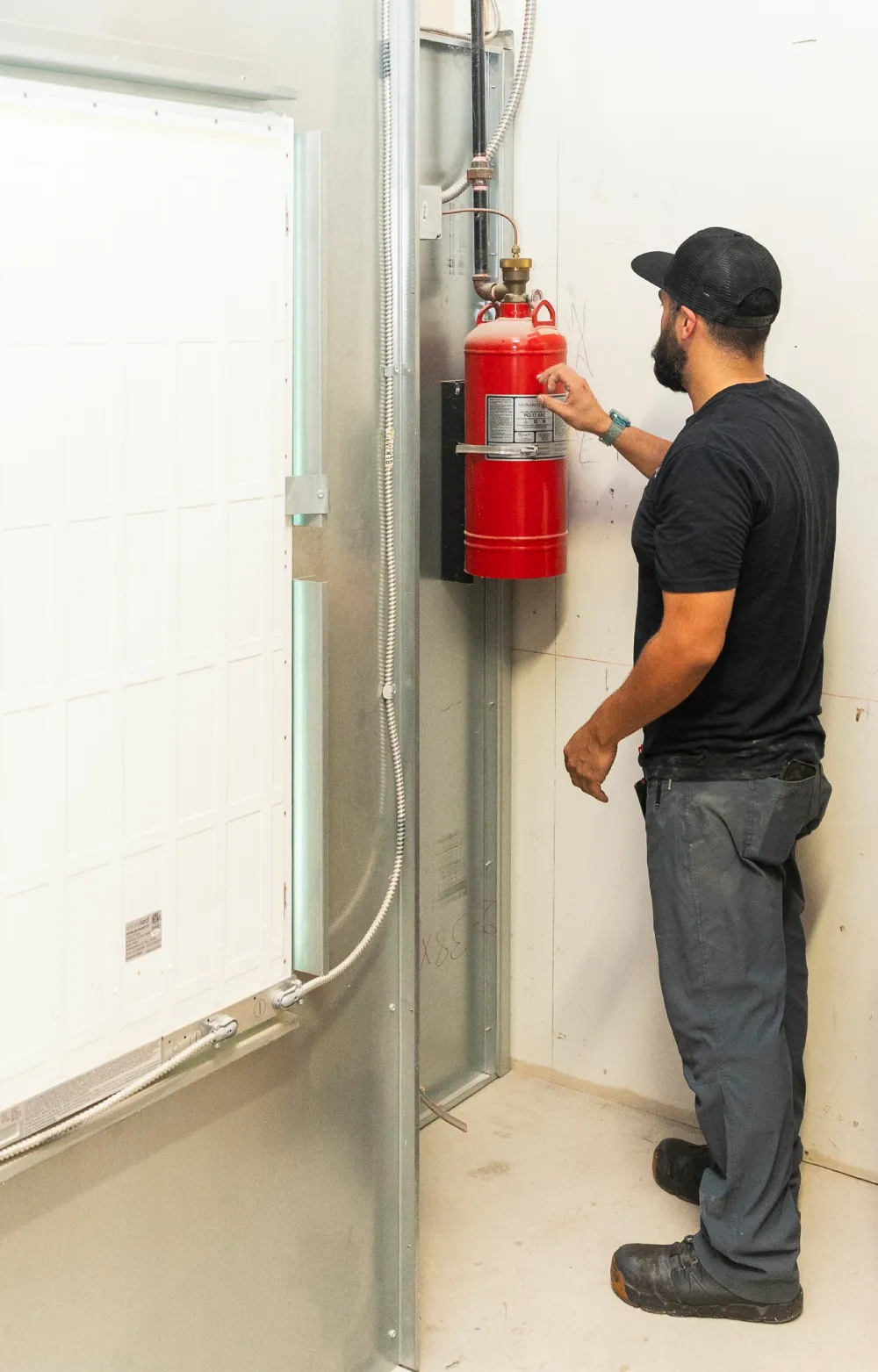 Technician inspecting a wall-mounted fire extinguisher in a hallway