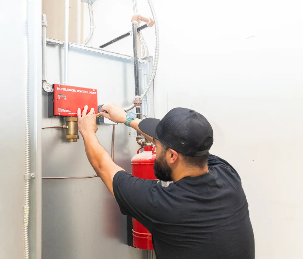 Technician inspecting a fire extinguisher beside a fire alarm pull station