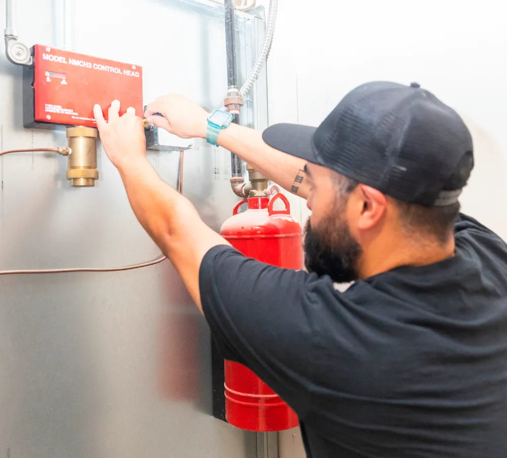 Technician inspecting a wall-mounted fire extinguisher beside a fire alarm pull station
