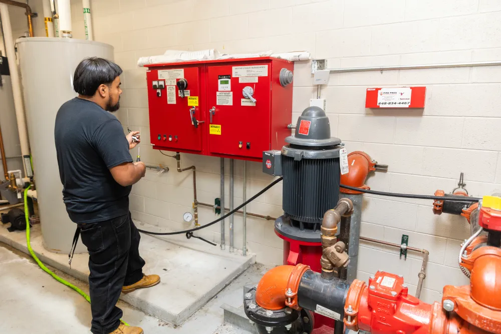 Technician inspecting a fire pump controller and piping