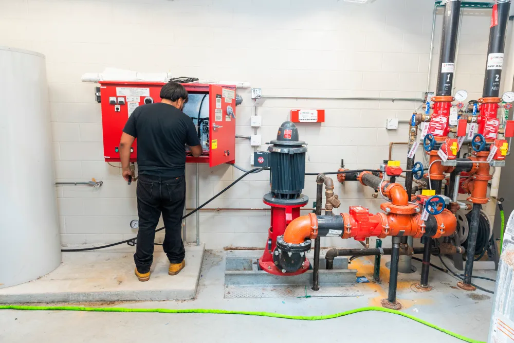 Technician servicing fire pump and sprinkler riser piping in a mechanical room