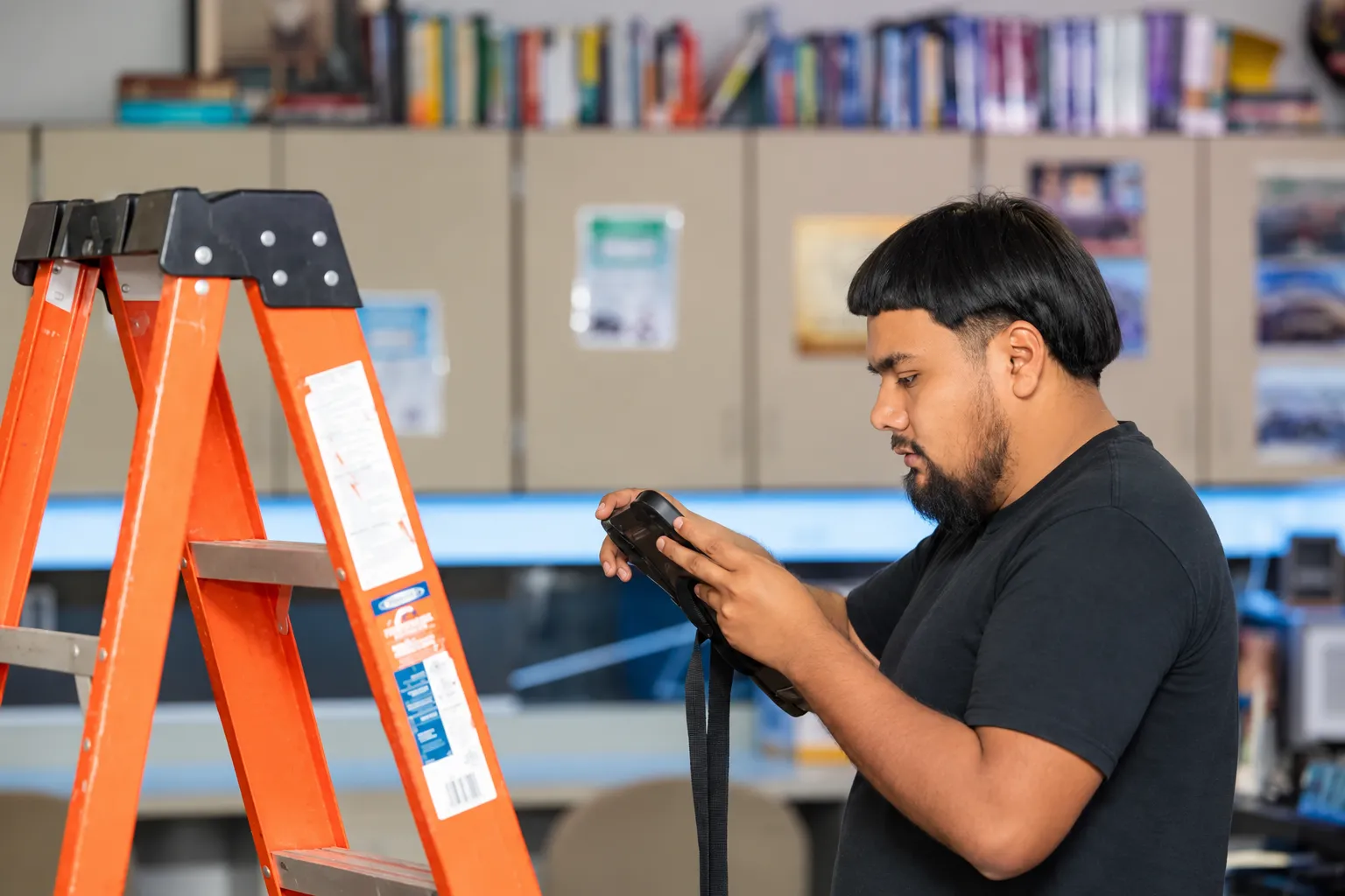 Technician using a tablet beside an orange ladder in a workshop